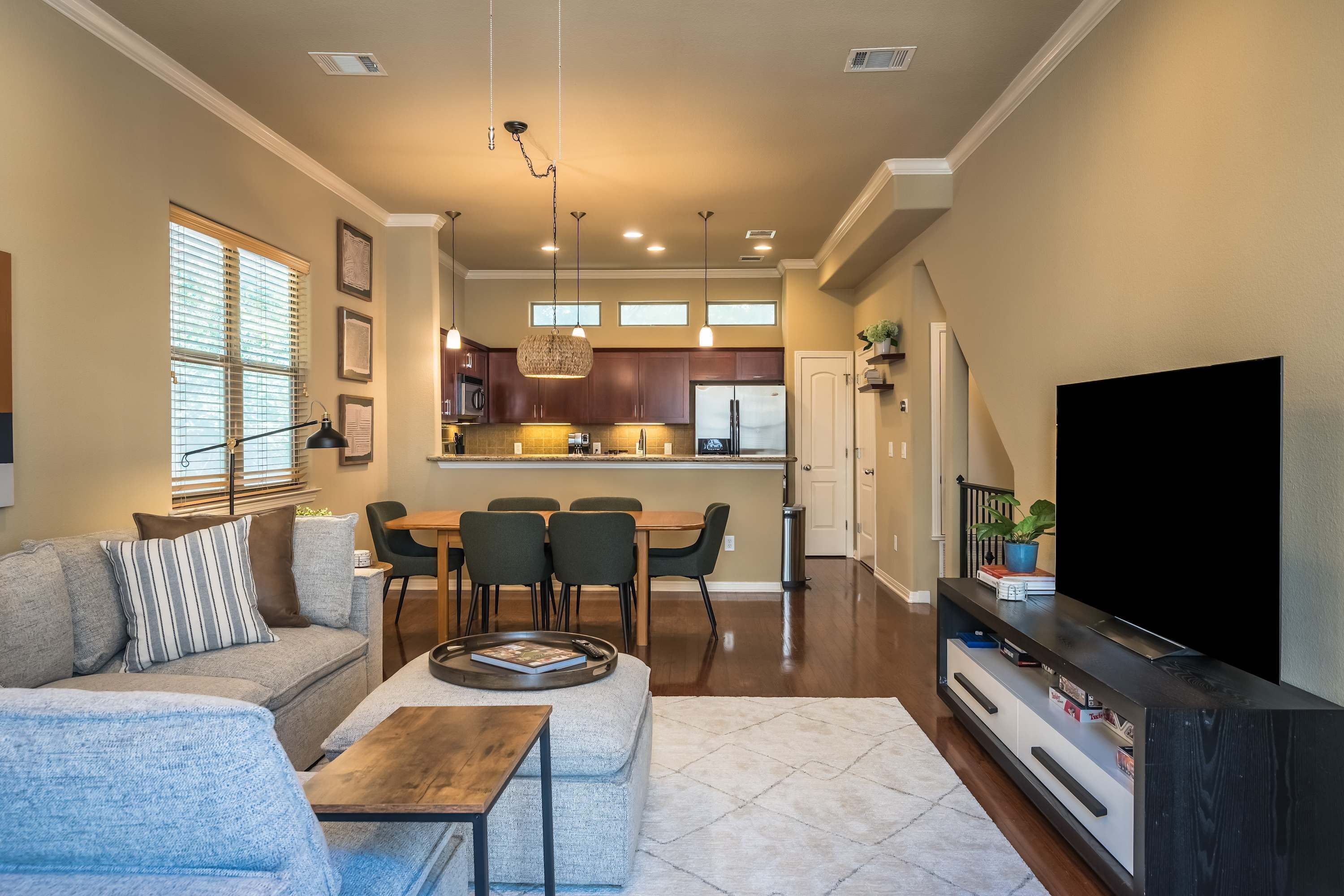 A modern living room with a sofa, coffee table, TV stand, dining area, kitchen, and a staircase leading to another level.