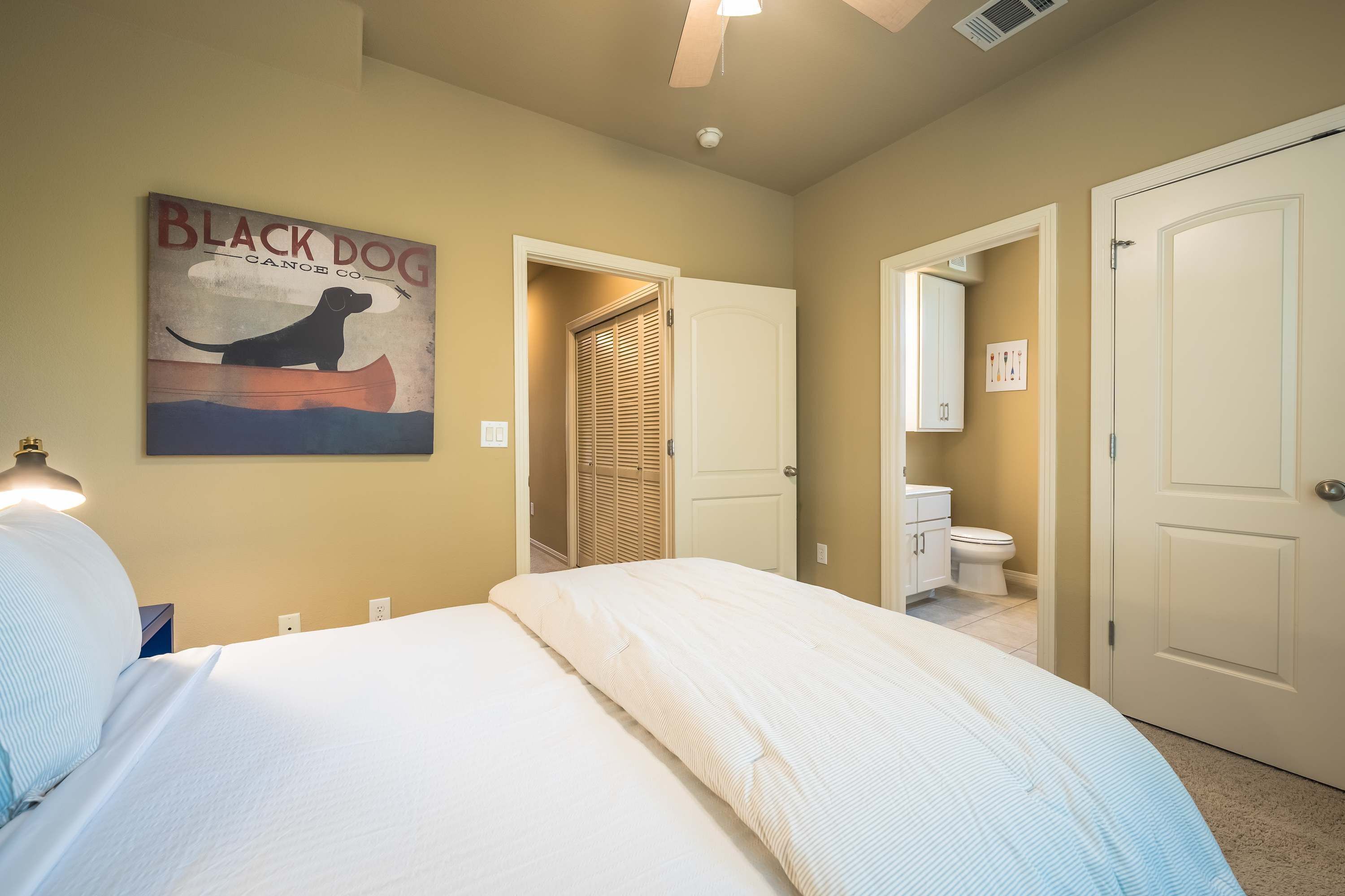 Un dormitorio con cama, una lámpara de pared, una puerta y un baño visible a través de una puerta abierta.