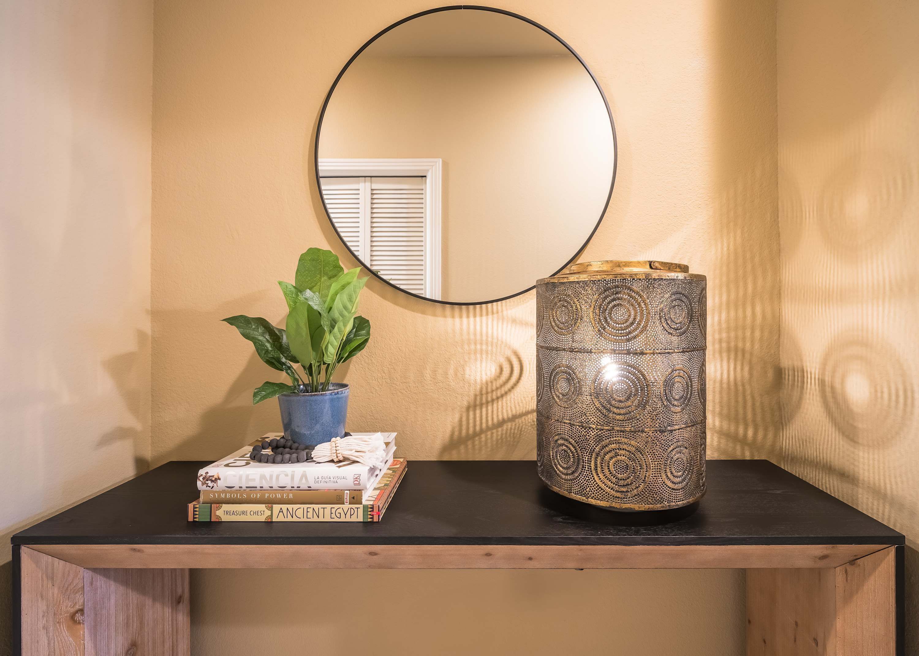 Un banc en bois agrémenté d’un miroir, d’une plante en pot et d’objets décoratifs, notamment des livres et un vase à motifs.