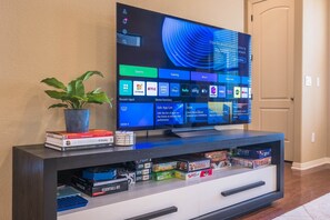 A flat-screen TV on a modern entertainment center with a plant, books, and board games. - Modern 3BR Townhouse Near Zilker Park (Austin)