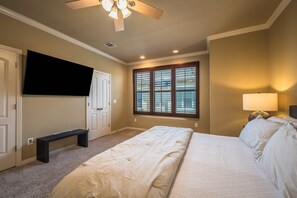 Ein Schlafzimmer mit Bett, einer Bank, einem Fernseher, einem Fenster mit Jalousien und einem Deckenventilator.
