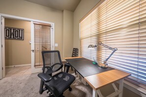 Ein Arbeitszimmer mit Schreibtisch, zwei Stühlen, einer Lampe und Jalousien am Fenster.