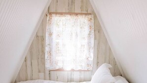 Une pièce triangulaire comprenant un lit, une fenêtre ornée de rideaux à motifs floraux et un mur en bois.