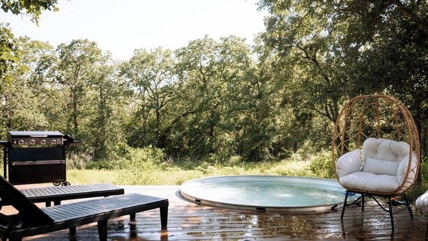 Une terrasse en bois avec un jacuzzi, un barbecue et un fauteuil en osier.