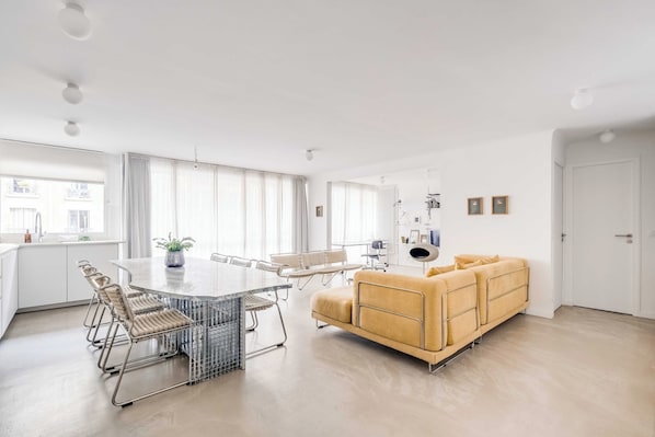 A modern living space with a dining area, sofa, and large windows.