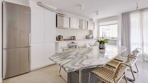 A modern kitchen with white cabinets, a marble island, and a stainless steel refrigerator. - Modern 1bdr/2p Flat With a Balcony - Menilmontant (Paris)