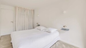 A bedroom with a bed, curtains, a door, and two wall-mounted lamps. - Modern 1bdr/2p Flat With a Balcony - Menilmontant (Paris)