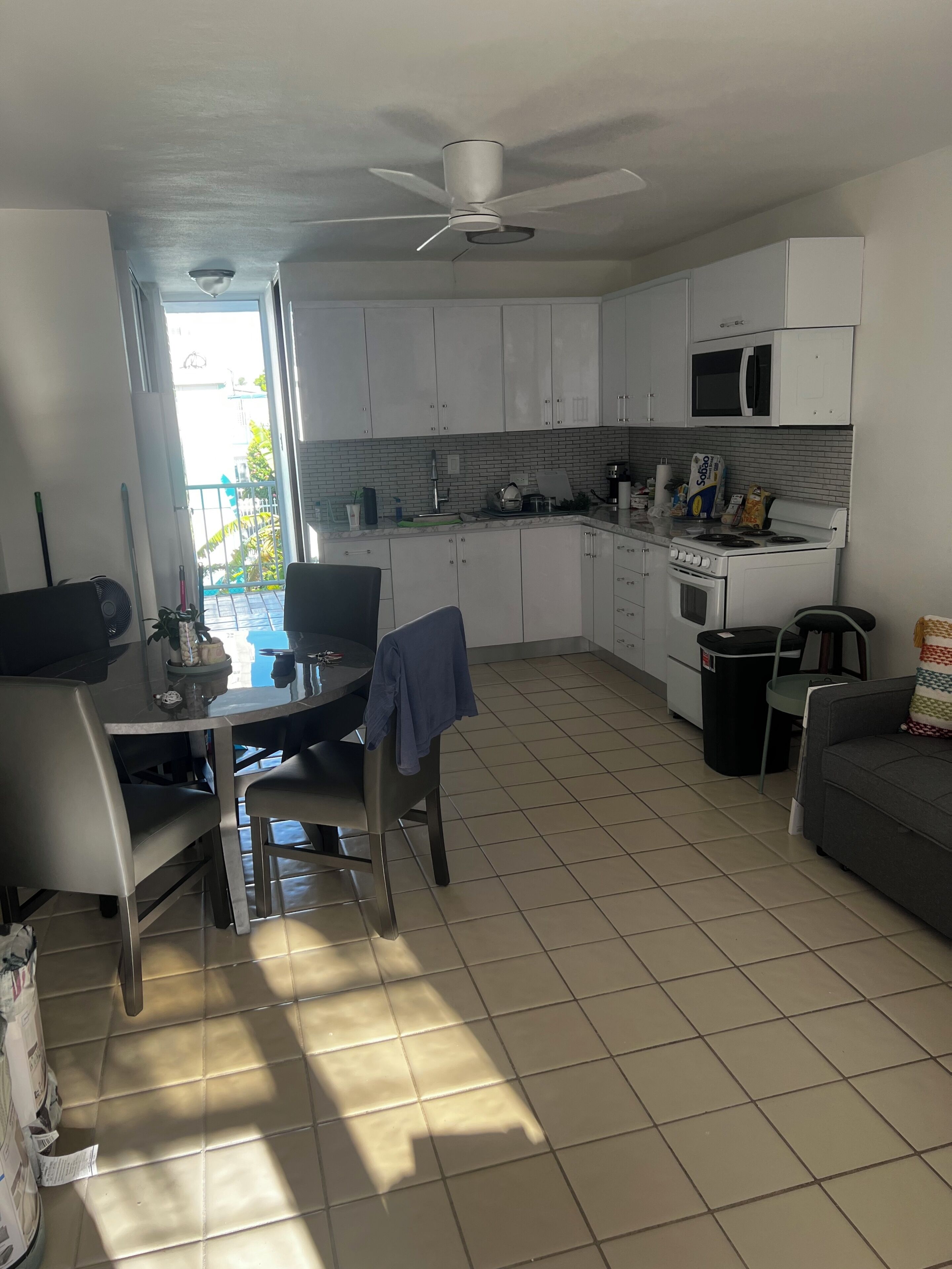 A compact kitchen with white cabinets, a microwave, and a gas stove. There is a dining area with a table and chairs, and a ceiling fan.