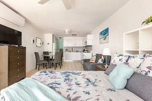 A bedroom with a bed, a dresser, a TV, a desk with chairs, and a kitchenette in the background. - Calm Cove Retreat a unique accommodation next to beautiful beaches Luquillo, PR. (Luquillo)