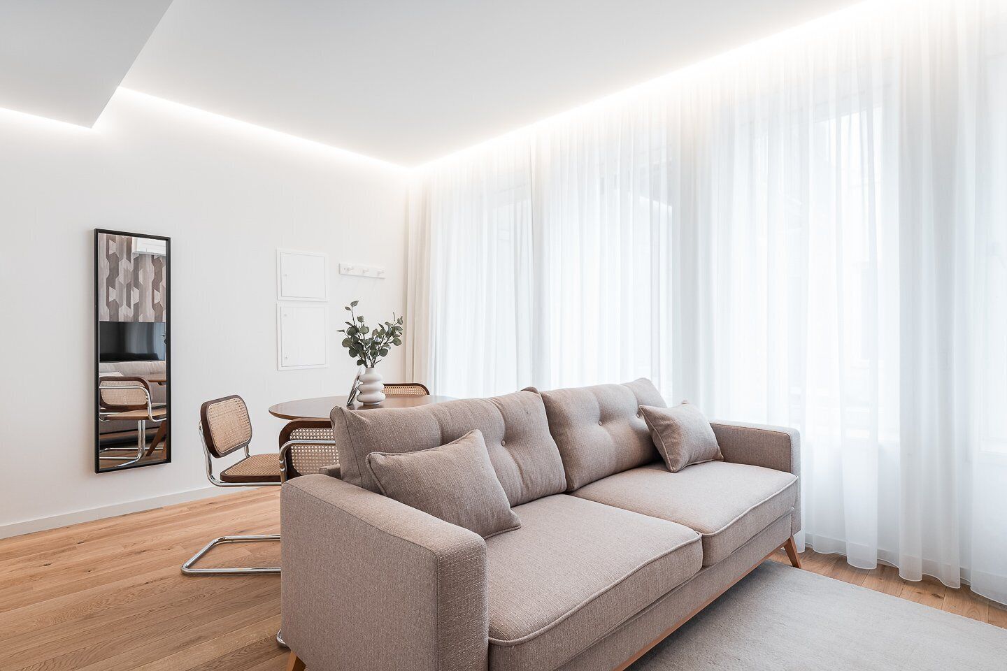 Un salon moderne avec un canapé beige, une table basse en bois et un coin repas avec des chaises.