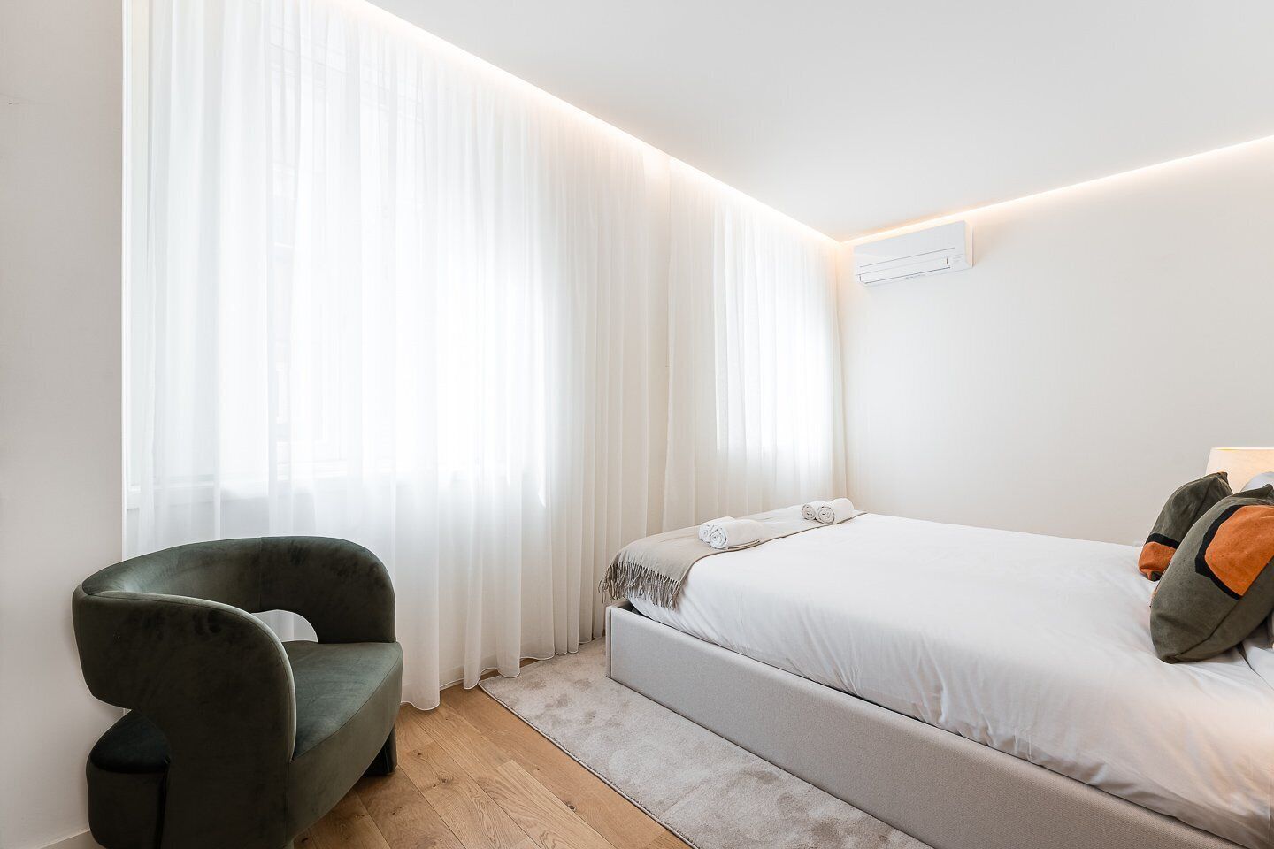 Un dormitorio moderno con una cama, una silla y cortinas translúcidas.