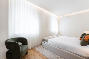 A modern bedroom with a bed, a chair, and sheer curtains. - GuestReady - Golden Formosa (Porto)