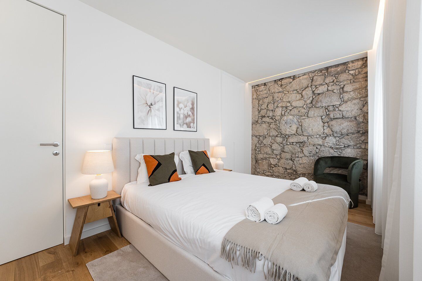 Een slaapkamer met een bed, twee bedlampen, een nachtkastje, een stoel en een stenen muur.