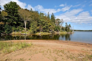 Paisagem natural com uma praia arenosa, um lago calmo e uma floresta densa.