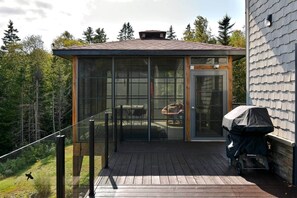 Ein überdachter Außenbereich mit Grill und Blick auf eine bewaldete Gegend.