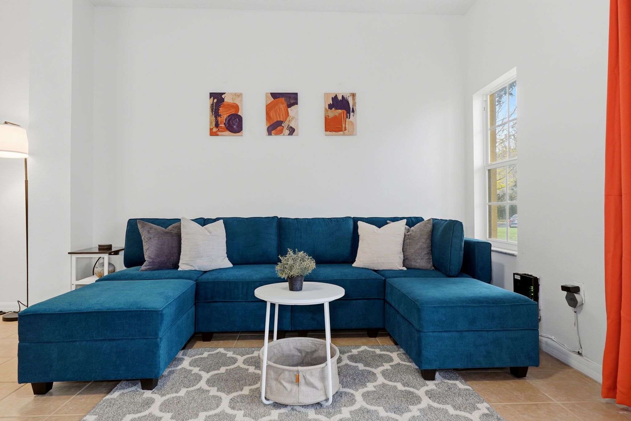 A modern living room with a teal sectional sofa, a small white table with a plant, and abstract art on the wall.