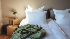 En pænt redt seng med hvide sengetæpper, et grønt tæppe og et trænatbord med en lampe.