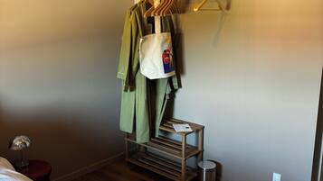 Hotelkamer met een bed, een houten vloer, een kapstok, een tafeltje met een tas en een prullenbak.
