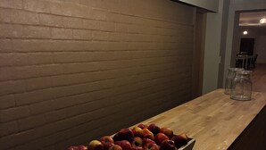 En træbordplade med en bakke æbler, en murstensvæg og hængende pendellamper.