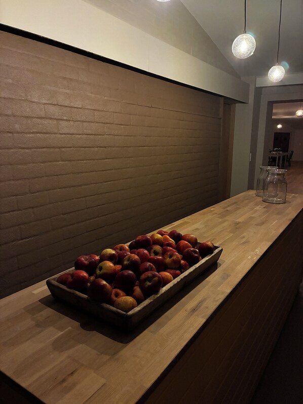 A wooden counter with a tray of apples, a brick wall, and hanging pendant lights. - Albi's Sandvig (Allinge)