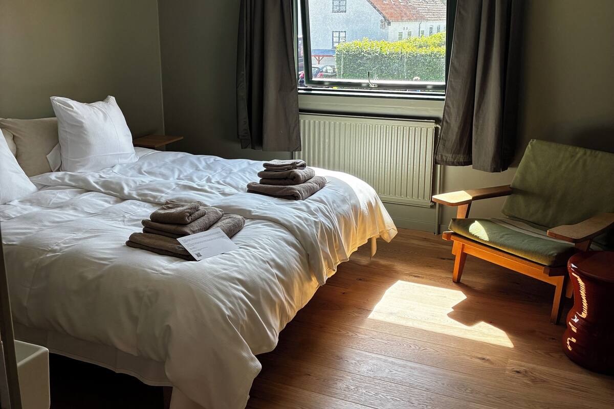 A bedroom with a bed, a chair, a window, and a radiator.