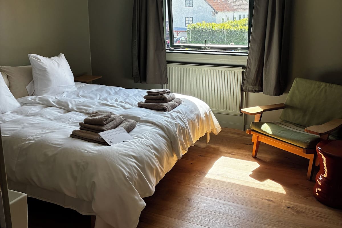 A bedroom with a bed, a chair, a window, and a radiator.