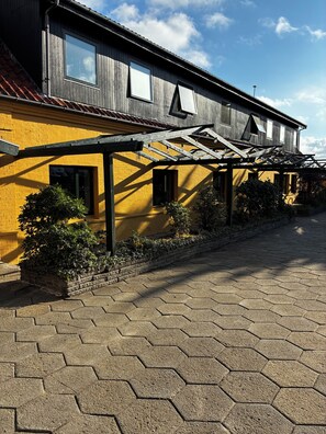 A building with a yellow facade, a covered outdoor area with hexagonal paving, and a clear sky.