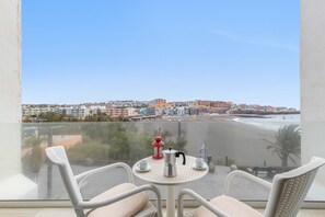 A balcony with a table, chairs, a red lantern, and a view of a beach and cityscape.