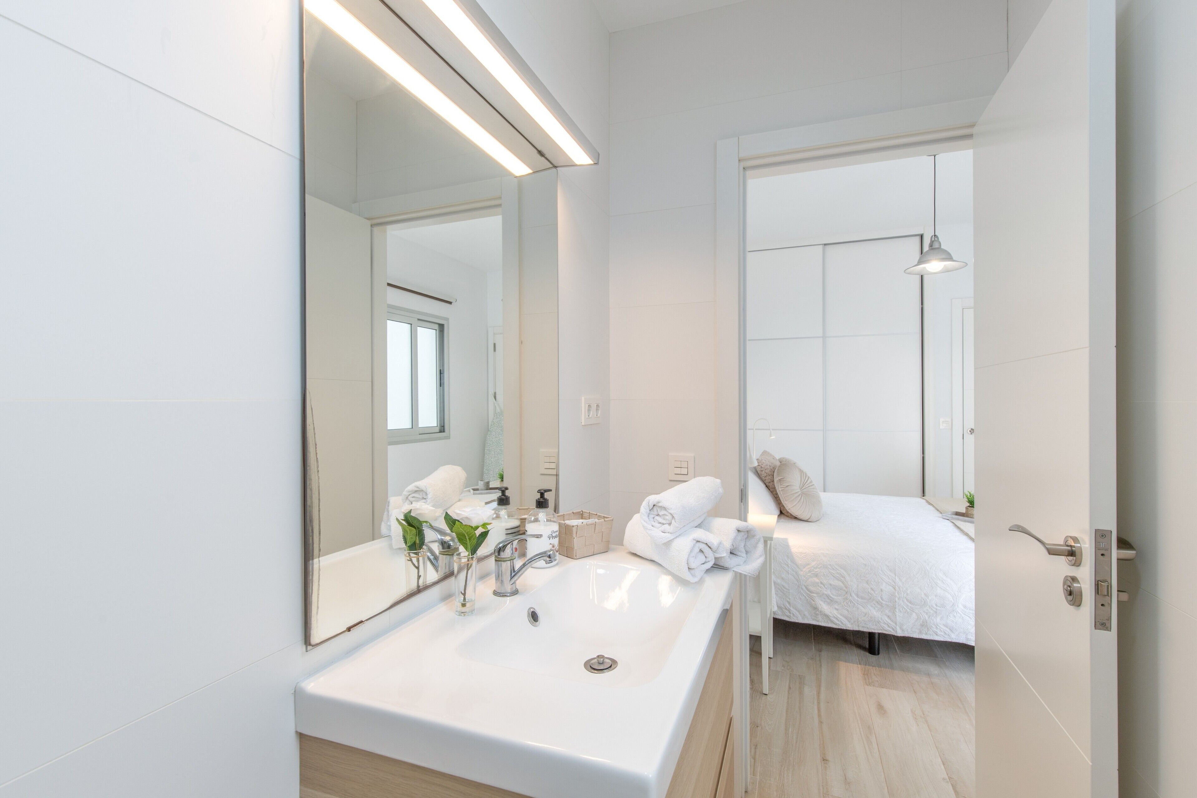 Une salle de bain moderne avec un grand miroir, un lavabo blanc et un lit avec une literie blanche.