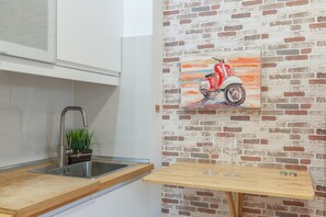 A kitchen with a sink, a potted plant, a table with a glass, and a brick wall.