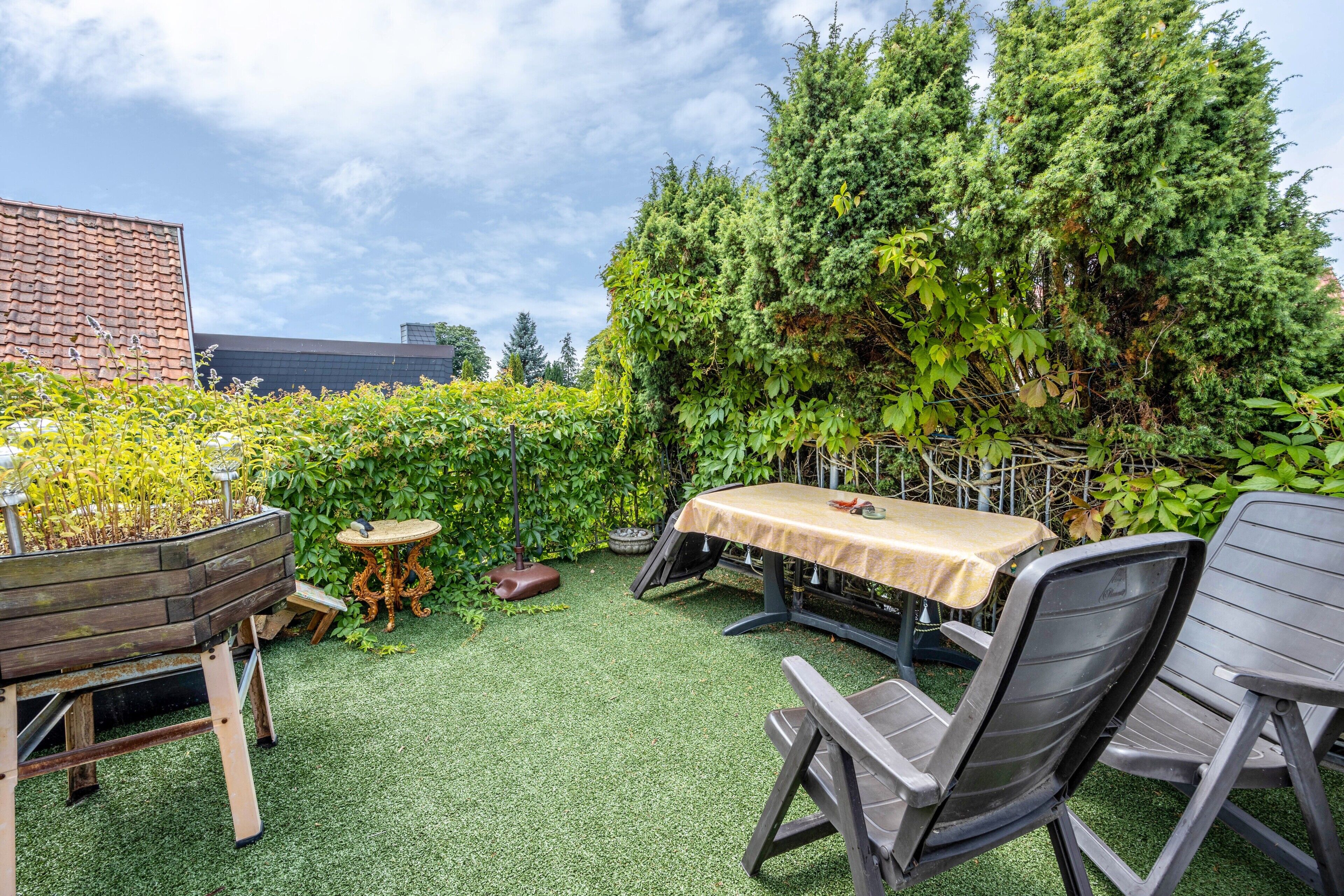 An outdoor patio area with a table and chairs, surrounded by lush greenery and a brick wall.