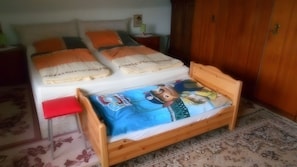A bedroom with two beds, a wooden wardrobe, a nightstand with a lamp, and a floral carpet. - Apartment 'Für 3 Personen 60 M²' with Shared Garden, Balcony and Wi-Fi (Harzgerode)