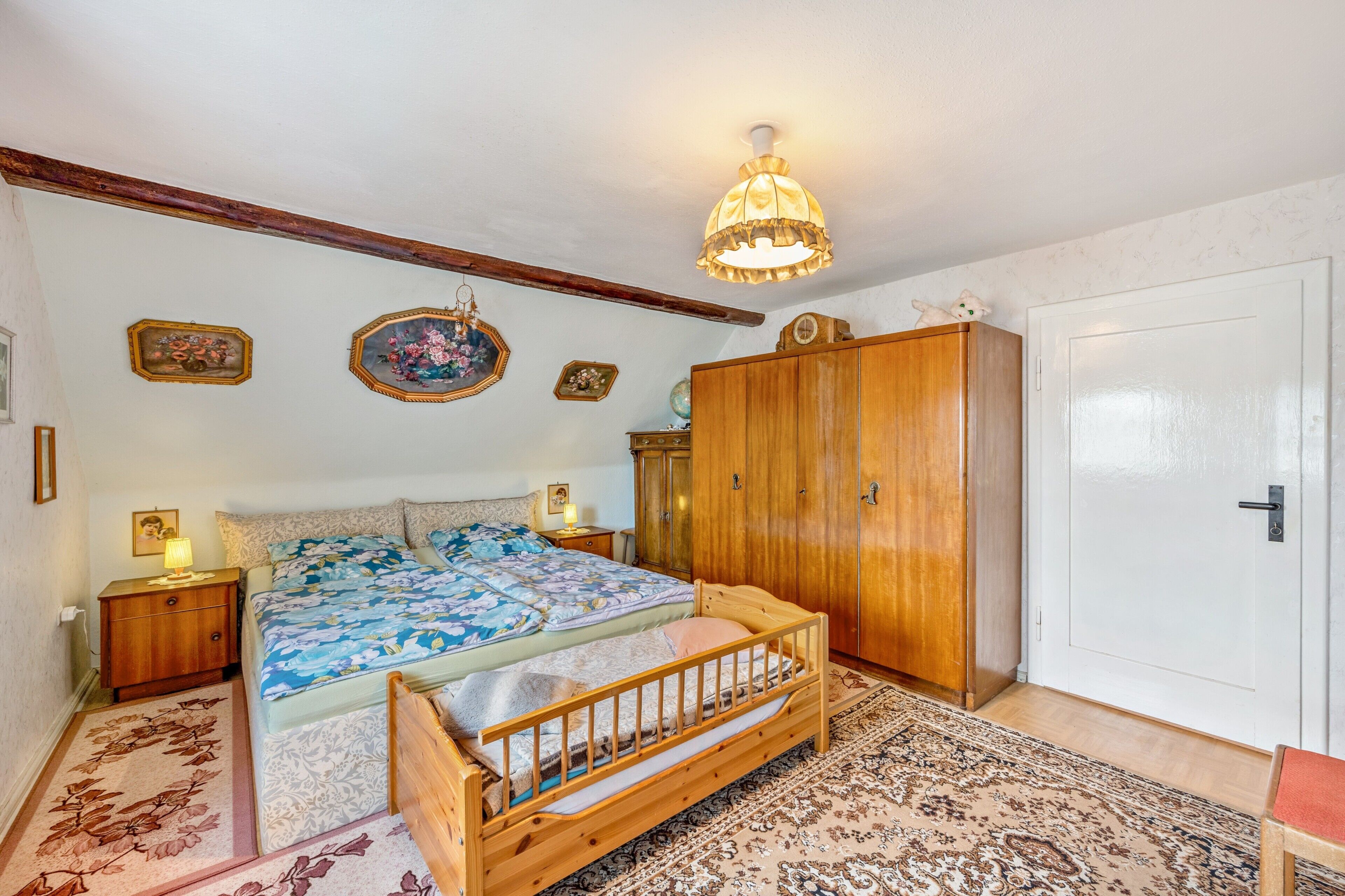 A bedroom with a wooden bed, a wardrobe, a nightstand, and a hanging lamp.