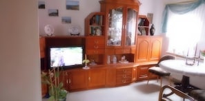 Una sala de estar con televisor, un mueble de madera y una mesa redonda con sillas.