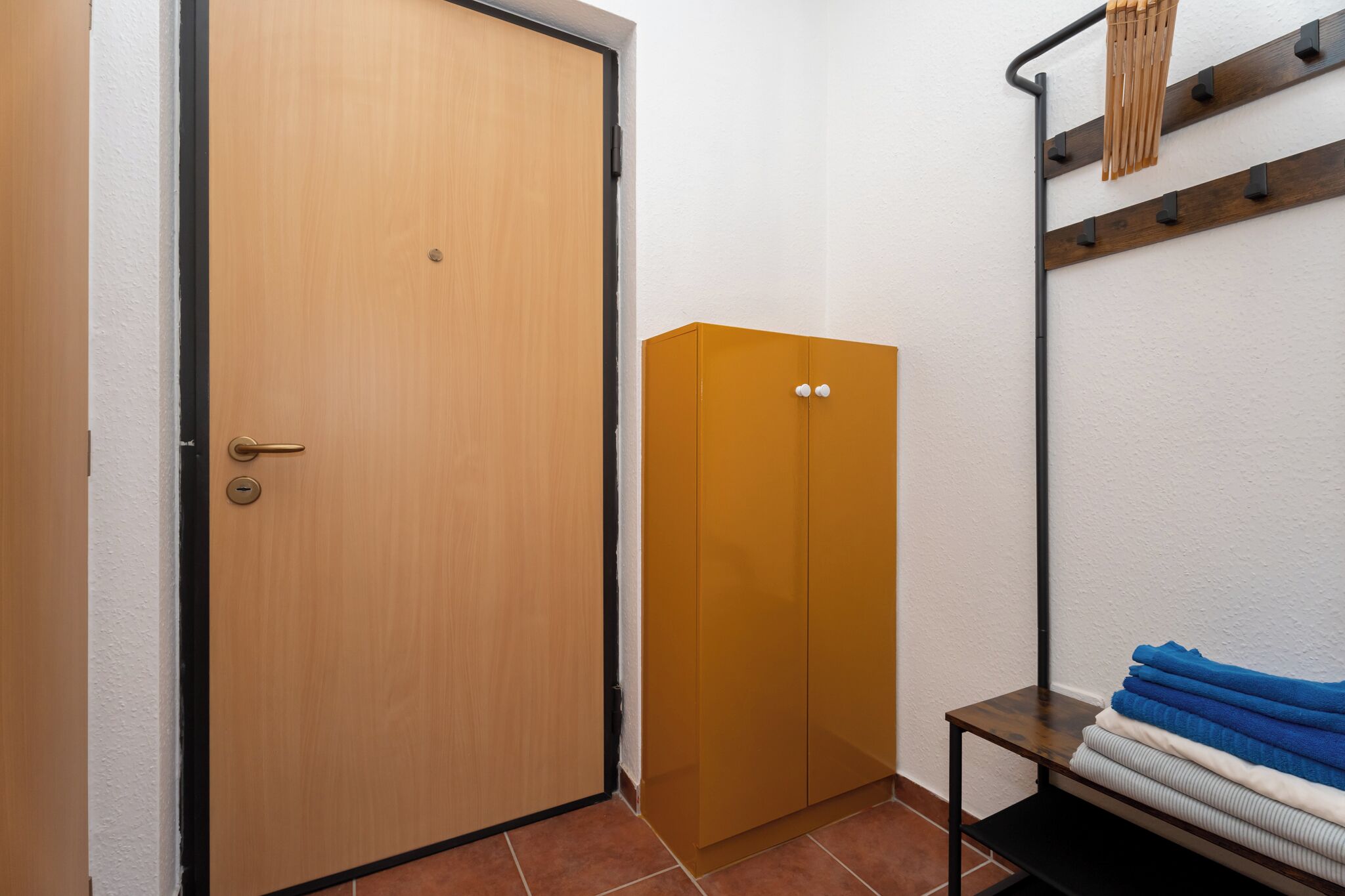 A room with a wooden door, a wardrobe, and a bench with folded towels.