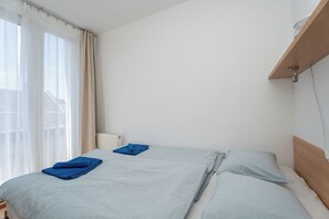 Ein Schlafzimmer mit einem Bett, einem Heizkörper, einem Fenster mit Vorhängen und einem Holzregal.