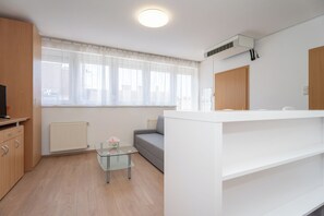 Ein modernes Zimmer mit einer Couch, einem Glastisch mit einer Vase, einem Heizkörper, einem weißen Schrank und einem Fenster mit Vorhängen.