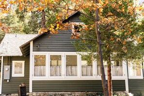 A house with a gabled roof, white-framed windows, and a stone foundation. - Charming, Vintage & Authentic Getaway - Sunroom - Free Parking! (Forest Falls)