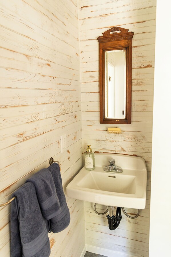 Un baño con paredes de madera, un lavamanos blanco, un espejo y un perchero para toallas.