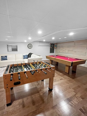 Une pièce équipée d’un baby-foot, d’une table de billard, d’un canapé et d’un jeu de fléchettes.