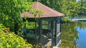 Een afgelegen hut met een glazen uitbouw, een terras en een steiger die uitstekt in een kalm meer, omringd door weelderige begroeiing.