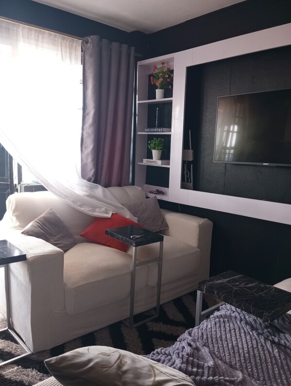A living room with a sofa, a small table, a TV, and a shelf with decorative items.