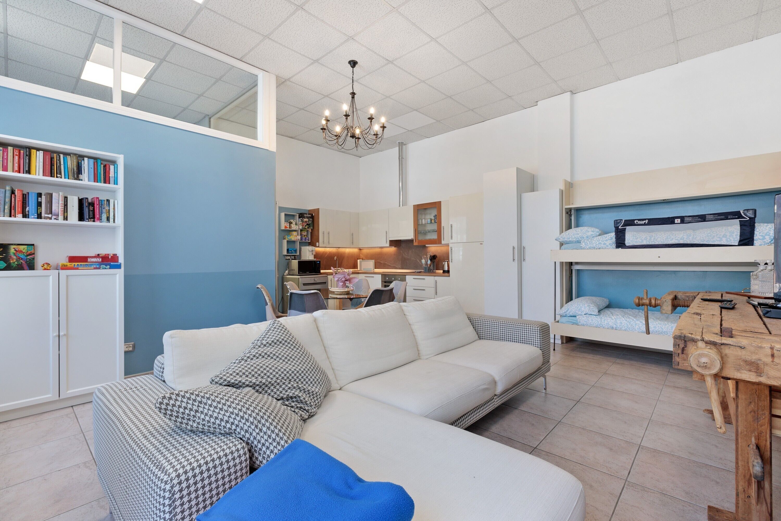 Un espacio habitable pequeño con sofá, estantería, kitchenette y literas.