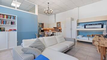 Un espacio habitable pequeño con sofá, estantería, kitchenette y literas.