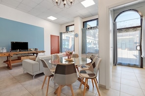 Un coin repas comprenant une table ronde en verre, des chaises rembourrées, un buffet en bois et un téléviseur.