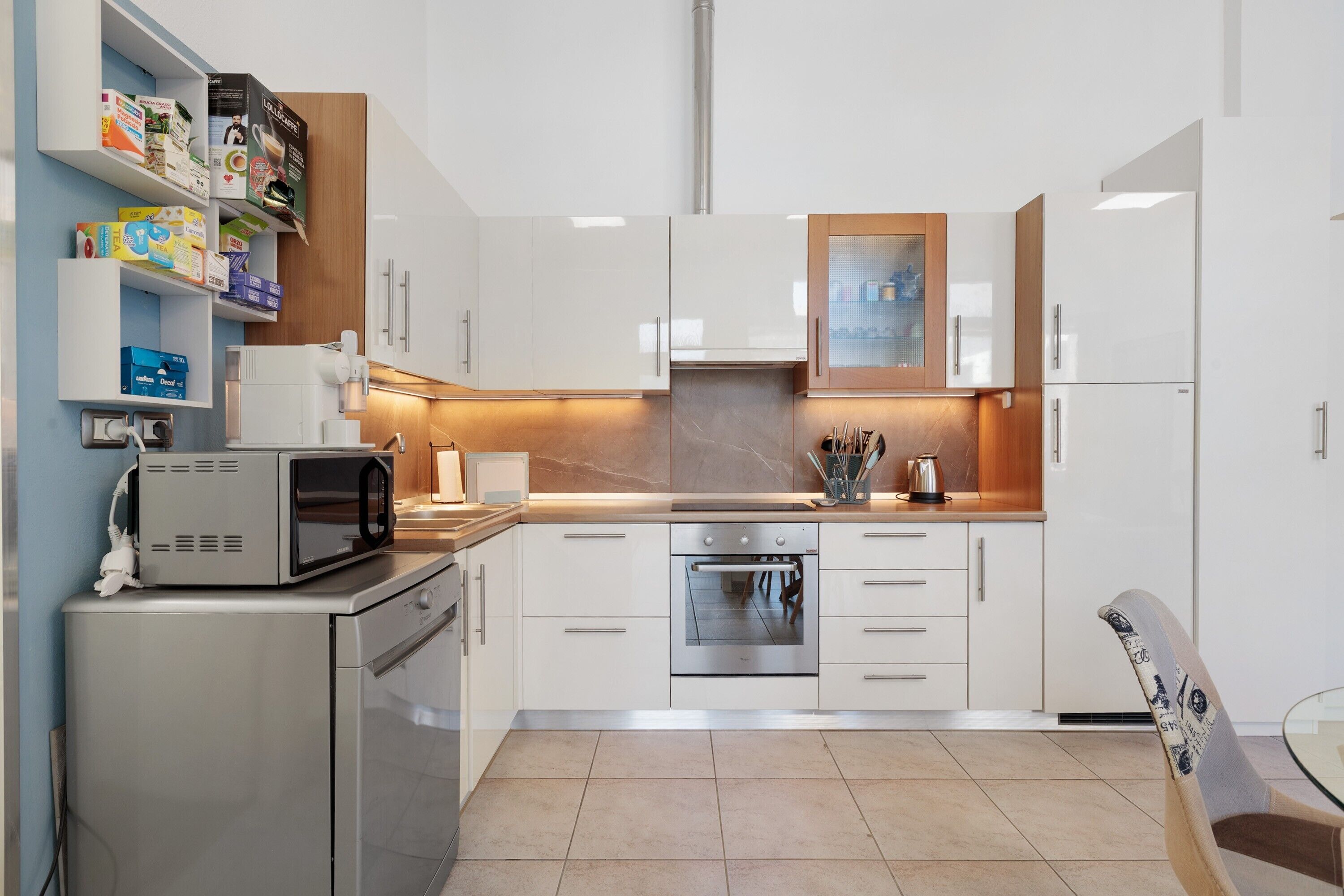 Una cocina moderna con armarios blancos, horno empotrado, microondas y cafetera.