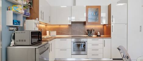 Una cocina moderna con armarios blancos, horno empotrado, microondas y cafetera.