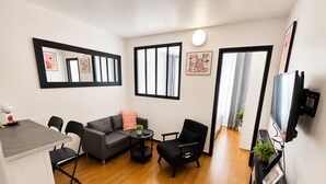 A modern living room with a grey sofa, black chairs, a small round table, and a TV mounted on the wall. - Cozy apartment just outside Paris – Clichy (Clichy)