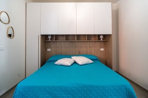 Quarto com cama, cabeceira branca e duas luminárias de cabeceira.