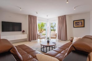 A spacious living room with leather sofas, a flat-screen TV, a round coffee table, and a large window with curtains. - Villa Principesa (Mandre)